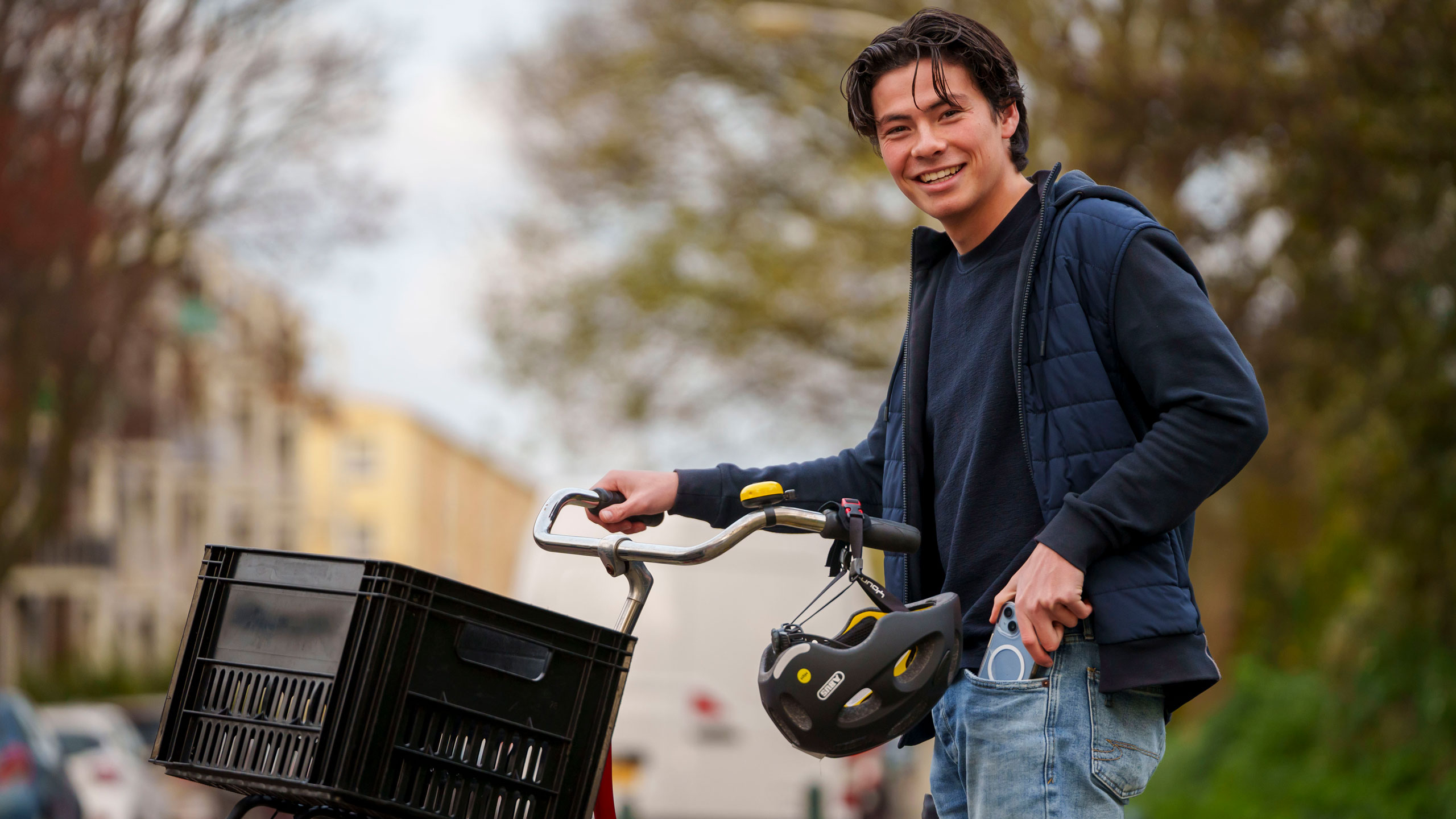 Jongere met fiets in de hand die mobiele telefoon in zak aan het steken is.