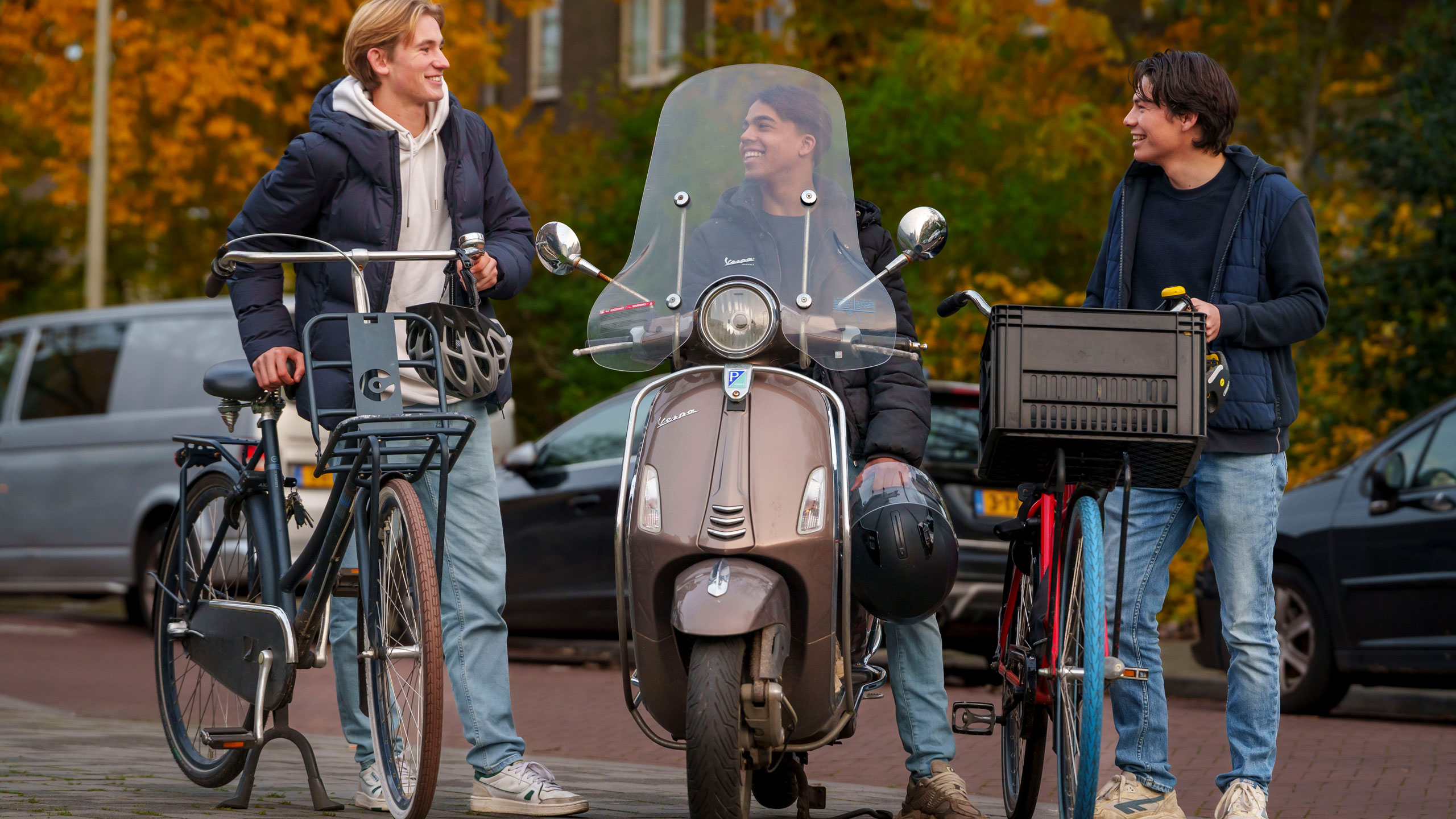 Drie jongeren naast elkaar op de stoep, 2 met hun fiets in de hand en 1 zittend op de scooter