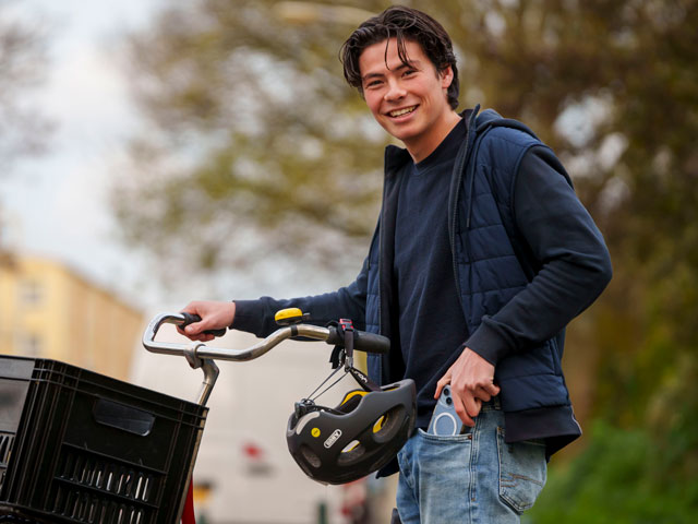 Jongere met fiets in de hand die mobiele telefoon in zak aan het steken is.