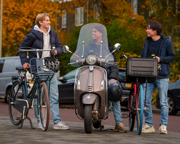 Drie jongeren naast elkaar op de stoep, 2 met hun fiets in de hand en 1 zittend op de scooter